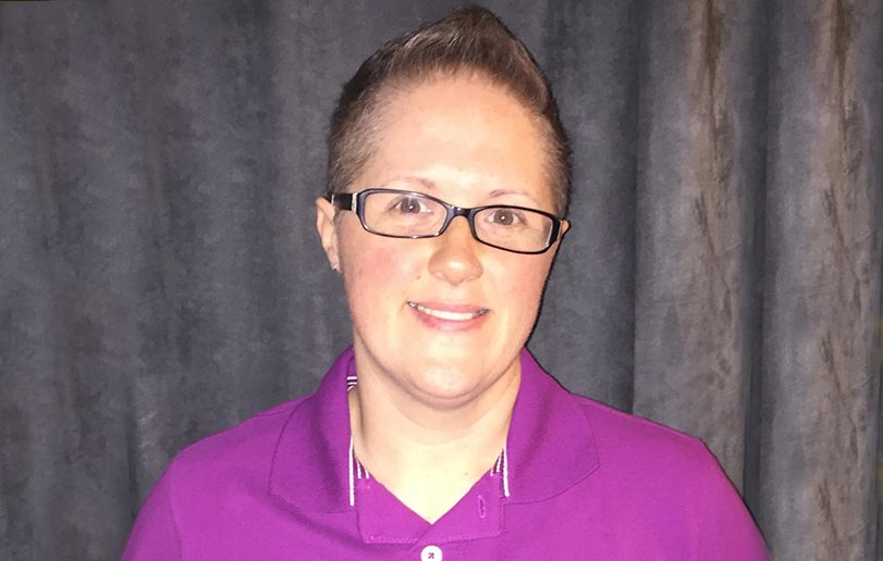 A woman in purple shirt and glasses smiling.