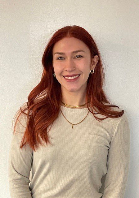 A woman with red hair standing in front of a white wall.